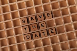 Top view of 'Save the Date' message using wooden letter blocks on a grid pattern background.