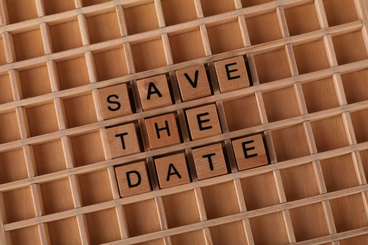 Top view of 'Save the Date' message using wooden letter blocks on a grid pattern background.